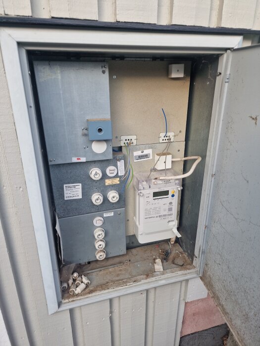 Öppet mätarskåp med huvudsäkringar och elmätare installerade, viserande kabeldragning och lediga säkringsplatser.