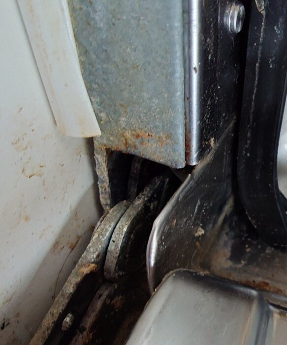 Närbild på gångjärnet till en diskmaskinslucka som visar tecken på rost och innebär problem med att hålla luckan stängd efter en olycka.