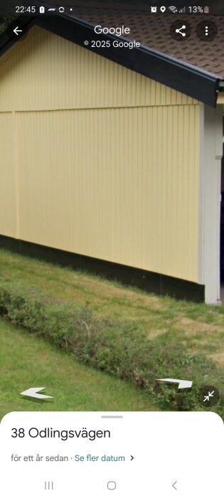 Gul yttervägg på ett hus med svart takfot och buskar i förgrunden, sett från sidan.