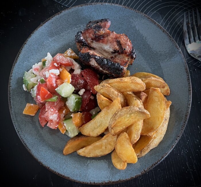 Grillat sidfläsk med klyftpotatis och en färgglad sallad med jordgubbar och fetaost serverad på en tallrik.