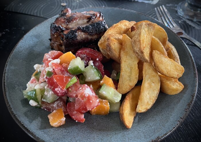 Grillat sidfläsk med klyftpotatis och sallad innehållande jordgubbar, fetaost och grönsaker på tallrik.