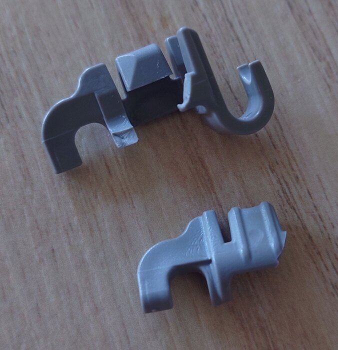 Två gråa plastfästen till en diskmaskinskorg på ett träbord.