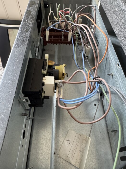 En ugns insida med flera färgade elkablar och komponenter anslutna, inklusive ett urverk, i ett metallhölje.