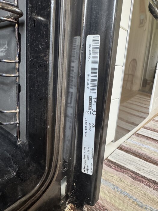 Invändig bild av ugnslucka med synlig etikett innehållande modellinformation och tekniska specifikationer.