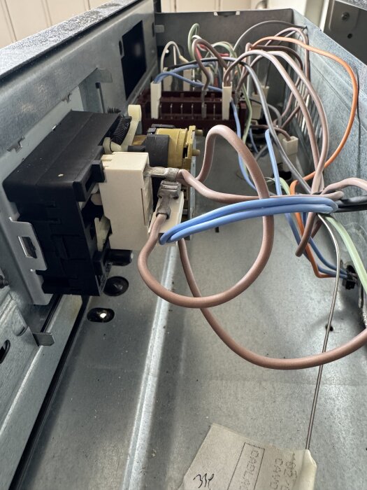 Insidan av en ugns elektroniska enhet med olika färgade kablar anslutna till komponenter.