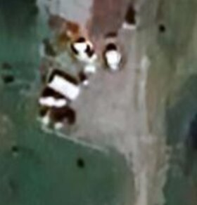 Luftfoto av tomt med grusbelagd yta, flera fordon och byggnader, omgiven av grönska.