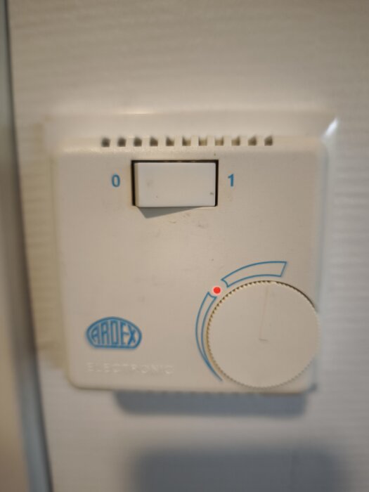 Ardex termostat med vridreglage och av/på-knapp, installerad på vägg. Saknar tydlig inställning för önskad temperatur.