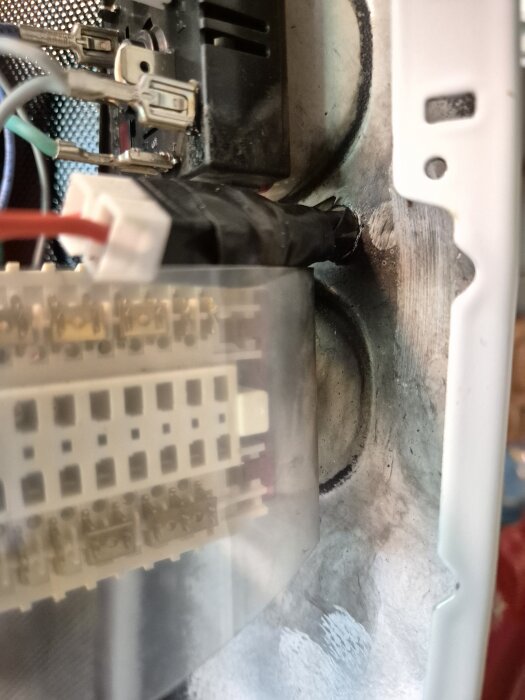 Närbild av en kontakt med flera kabelanslutningar, delvis täckt med eltejp, omgiven av sotfläckar på en metallyta.