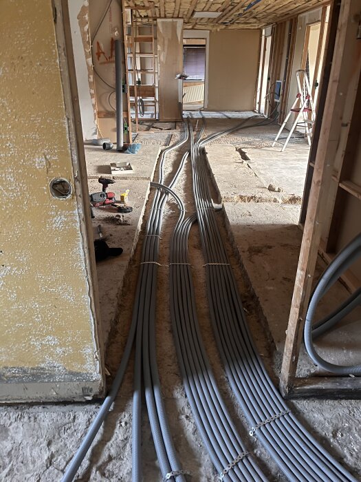 Grå rör i rör-system, lagda i marken under renovering av värmeledningar i byggnad. Oisolerade rör väntar på beslut om isolering.