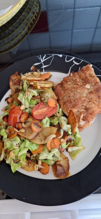 Tallrik med snitzel, råstekt potatis, morötter, tomater, kål och mungbönor.