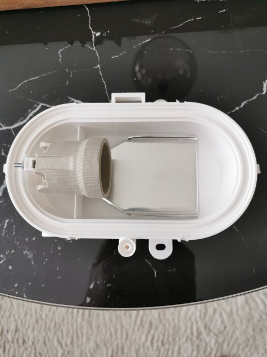 Vit, oval gallerarmatur IP54 på svart yta, insida synlig utan jordanslutning.