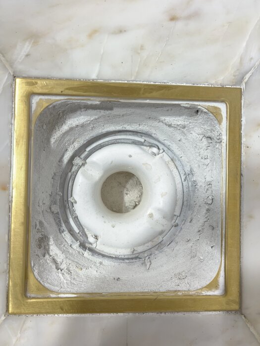 Golvbrunn med vit insats och kant av guld, omgiven av marmorkakel. Inlägg handlar om att säkerställa professionellt utfört arbete.