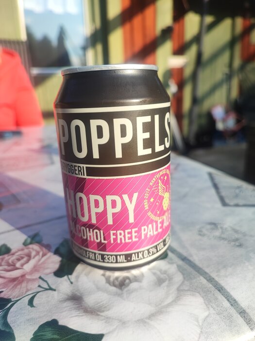 En burk Poppels alkoholfritt pale ale på ett blomdekorerat bord i solljus.