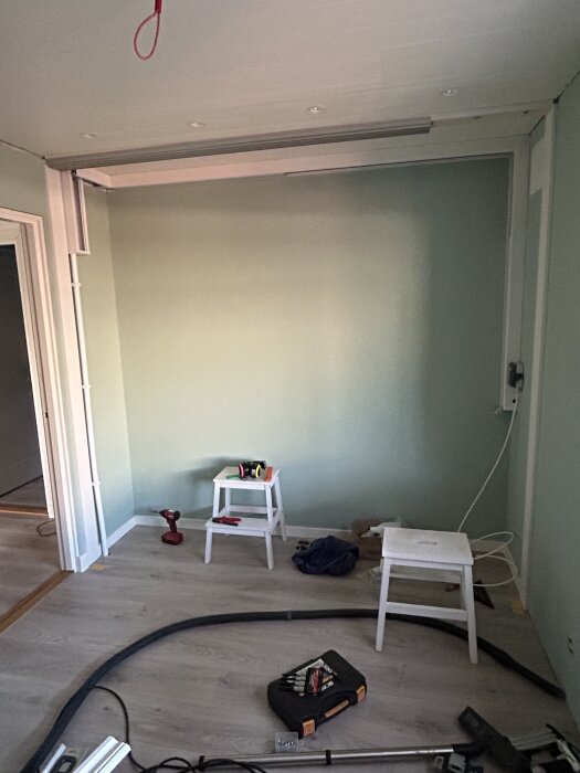 Renovering av rum med nytt golv, verktyg på pall, sladdar och kanaler synliga, förberedelse för skjutdörr och installation av belysning.