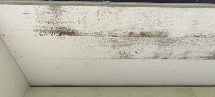 Färgade prickar och fläckar synliga på en vitmålad takfot utomhus.