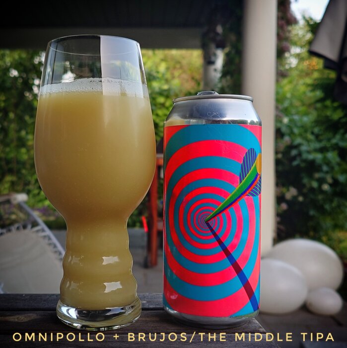 Ett glas med grumlig gul dryck och en färgglad burk med texten "Omnipollo + Brujos/The Middle TIPA". Bakgrunden visar en somrig uteplats.