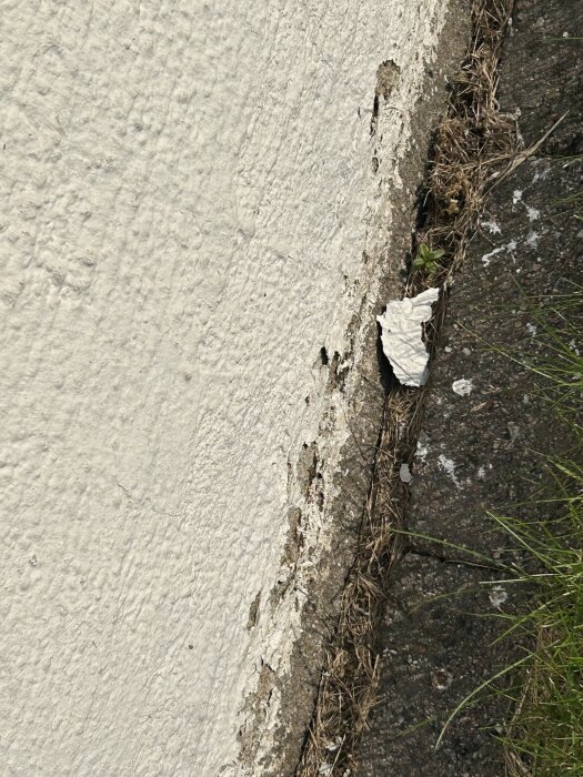 Putsad mur med avflagande färg nära marken, visar behov av underhåll och möjlighet till omputsning eller målning på nytt.