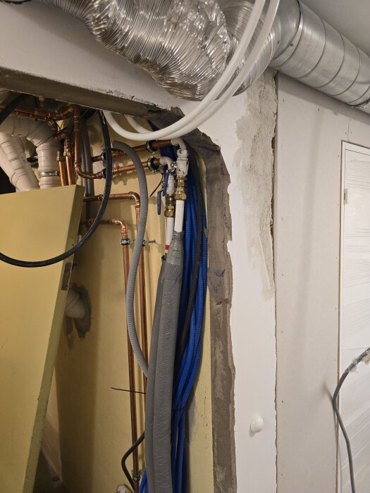 Rördragning och kablage synliga i öppningen av en vägg under rivning i källare, med flexibla ventilationsrör och kopparrör tydligt framträdande.