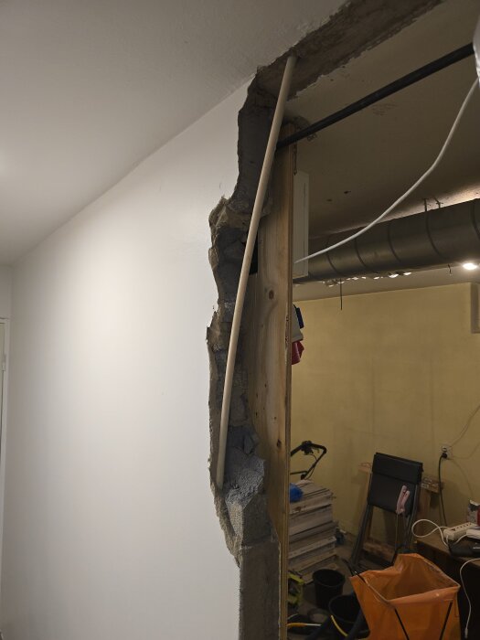 Vägg under rivning, delvis borttagen med blottlagt flexrör för ventilation och byggmaterial synligt i bakgrunden.