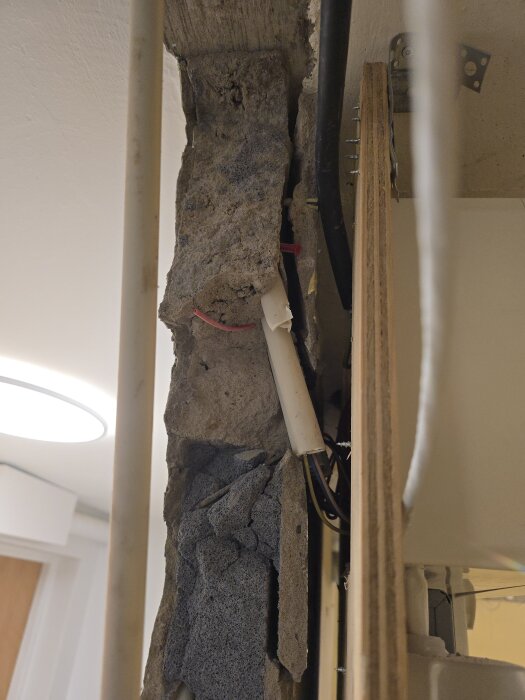 Sönderslagen blåbetongvägg med synliga rör och kablar under renovering.