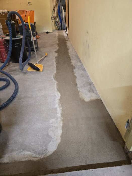 En nyslipad betonggång längs en vägg, med verktyg i bakgrunden. Betongen ser fortfarande färsk ut efter en dags arbete.
