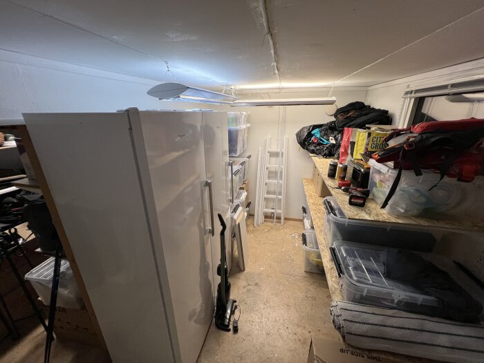Ordning i förråd med nya hyllor, fyllda med verktyg och förvaringslådor bakom en vit garderob i ett trångt utrymme.