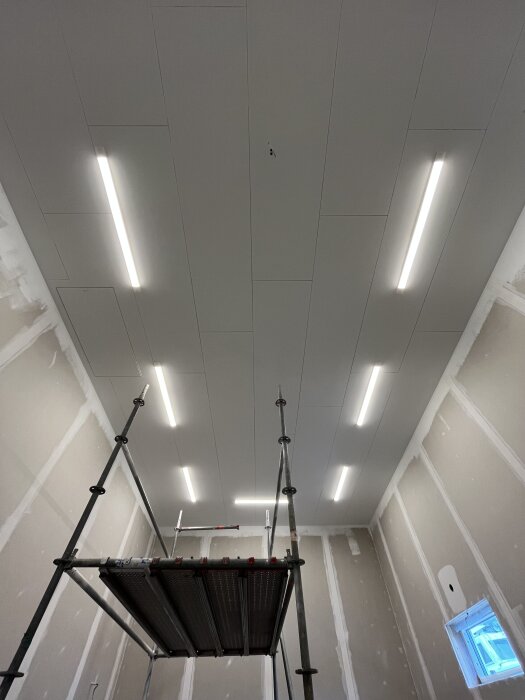 Tomt rum under konstruktion med vit takbelysning, byggnadsställning i mitten och oavslutade väggar.