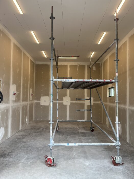 Byggarbetsrum med tom interiör och byggnadsställning under installation av belysning, redo för målning och andra avslutande arbeten.