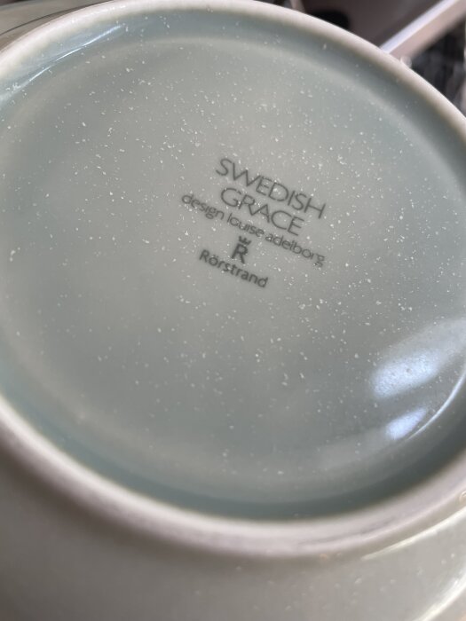 Tallrik med vit beläggning och prickar på ovansidan, text "Swedish Grace design Louise Adelborg Rörstrand" synlig.