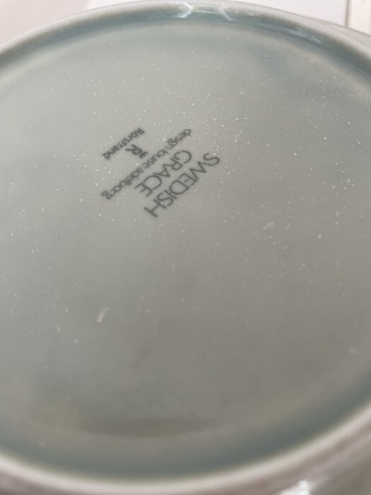 Baksidan av en tallrik med vit beläggning och prickar efter diskning, texten "SWEDISH GRACE" syns tydligt.