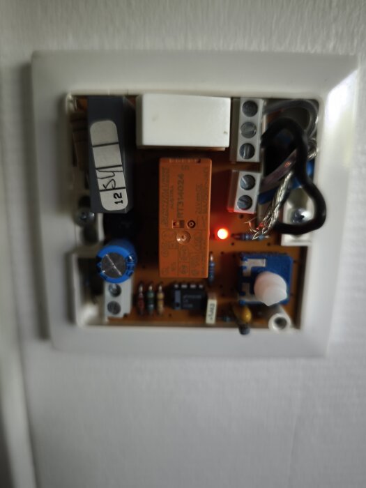 Elektrisk krets med lösa ledningar och röd indikatorlampa inuti en väggmonterad dosa.
