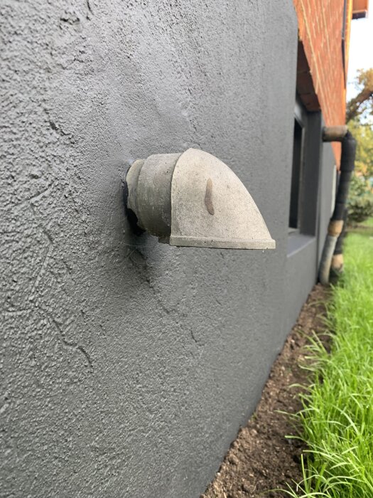 Ventilhuv fastsatt på grå vägg, ansluten till ett 60 mm rör som går genom väggen.