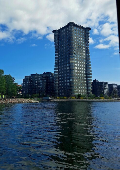 Höghus vid vattnet under en blå himmel, omgiven av lägre byggnader och grönska.