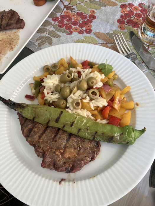 Grillad ryggbiff med rub och en stor grön sivripaprika på tallrik, serverad med paprikasallad, rödlök, oliver och dressing.