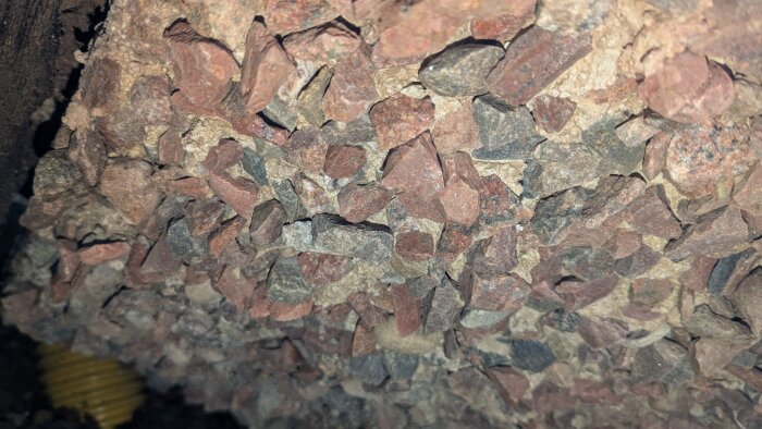 Bilden visar stenar och grus under en husgrund belyst med LED-lampa, där några svarta linjer också syns.