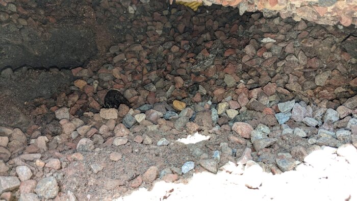 Stort grushål under husgrund med blandade stenar i olika storlekar. Svarta linjer syns på grund av belysning med LED-lampa.