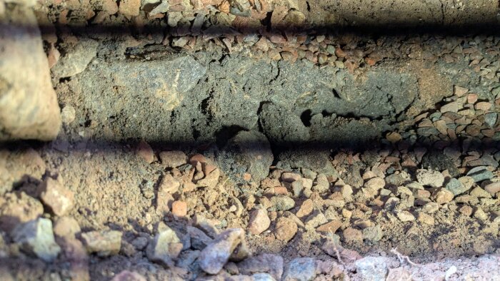 Hål under mark grund, grus och jord syns. Svarta linjer från LED-belysning. Möjlig risk för mögel eller skada.