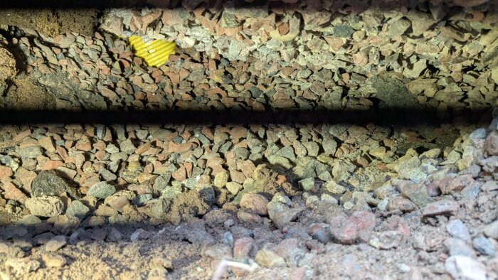 Grus och jord i ett hål under en betongplatta, vilket exponerar ett tomrum där en LED-lampa skapar svarta linjer.