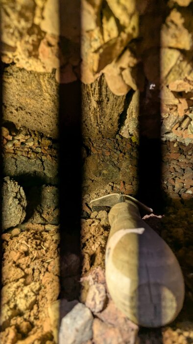 Ett hål under en husgrund med jord och sten, delvis exponerat, och ett verktyg i närheten. Svarta linjer från LED-ljus skär genom bilden.