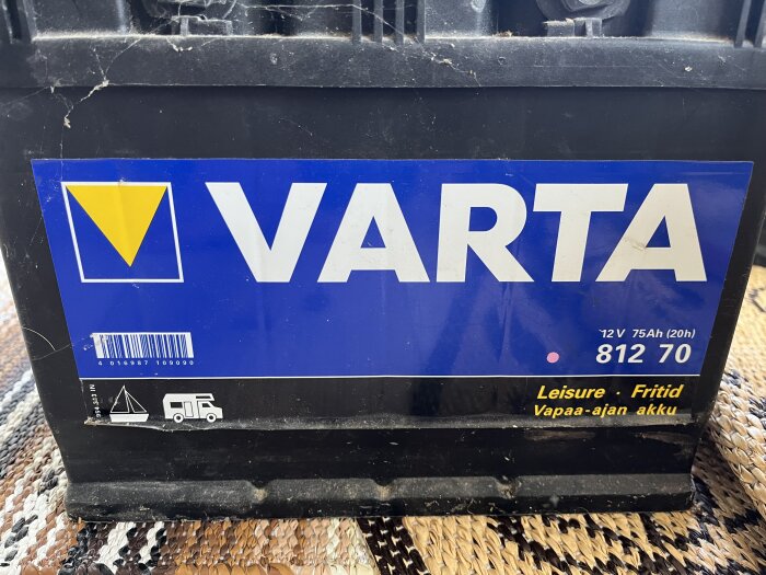 Varta fritidsbatteri med en etikett som visar specifikationerna 12 V, 75 Ah, placerat på en flätad matta.