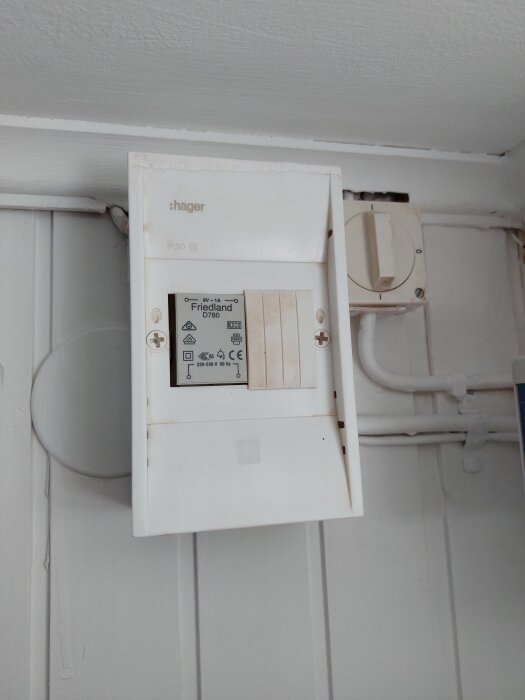 Elektrisk dörrsignal från Hager, modell Friedland D780, monterad på vit väggpanel i en källare.