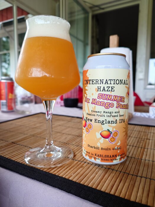 Ett glas med skummande New England IPA och en burk International Haze Mango Passion fruktöl står på en bordstablett.