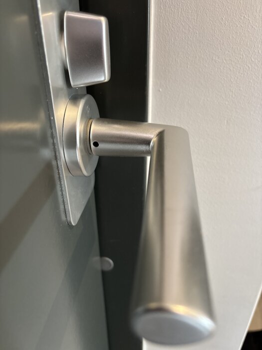 Dörrhandtag och vred på en metallisk dörr, med fokus på låsmekanismen.