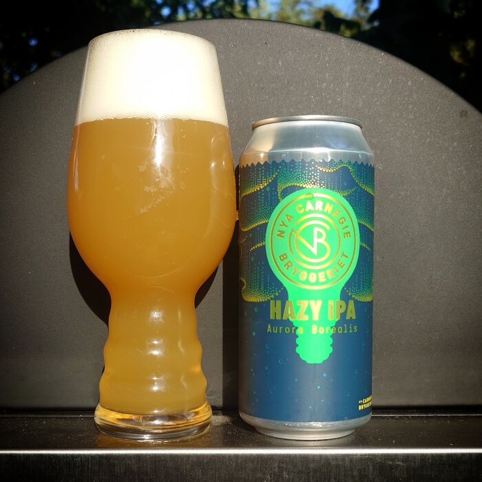 Ölglas med skummande Nya Carnegie Bryggeriets Hazy IPA framför en burk med etiketten "Aurora Borealis".