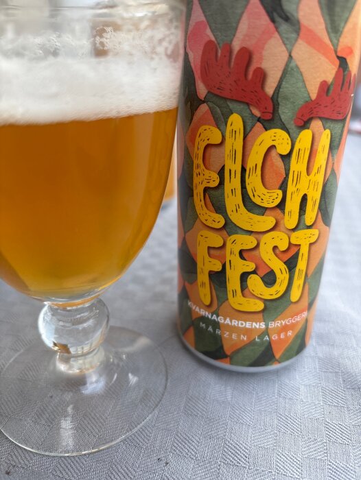 Ölglas med skummande lager bredvid en burk med färgglad etikett från Kvarnagårdens Bryggeri.