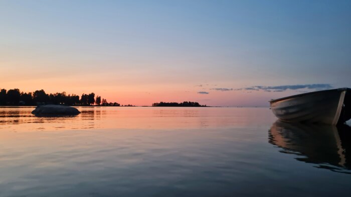 Båt vid strand i solnedgång, lugnt vatten och avlägsna träd på midsommarnatten 2025.
