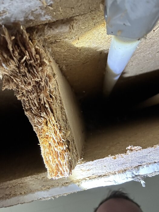 Bild av en träkonstruktion med synliga fibrer och ett rör, del av en köksvägg från ett 70-tals modulhus under renovering.
