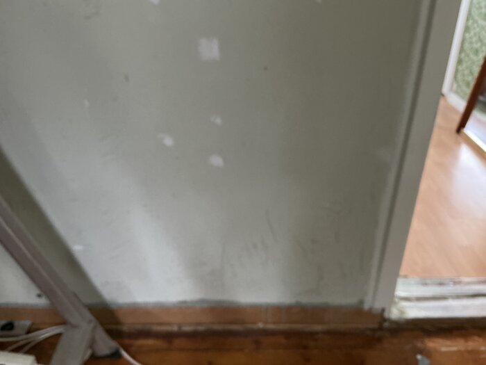 Vägg utan panel med gamla golvlister och dörrkarm i hall, redo för installation av bröstpanel Moelven och nya golvlister.