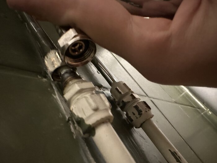 Hand justerar en sanitetsrörkoppling i ett badrum, med fokus på röranslutning som behöver adapter för 16.5 mm kranrör.