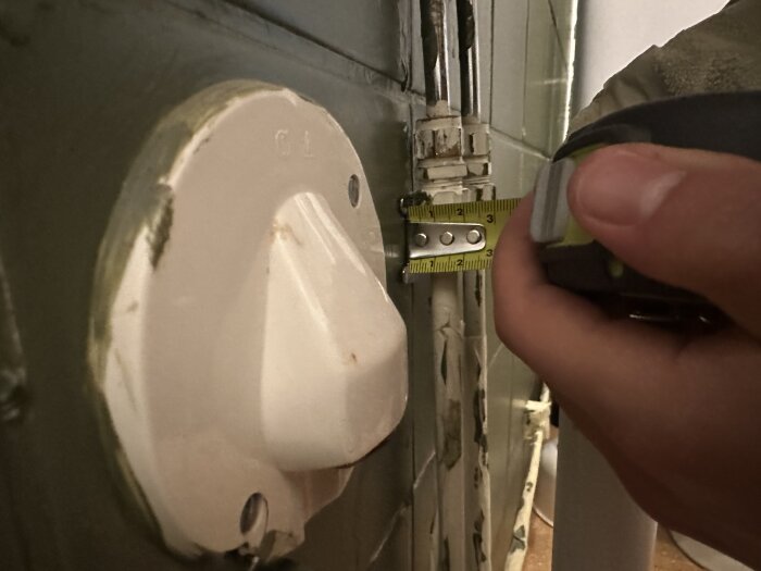 Mätning av ledningsrör med måttband framför en avstängningsventil i badrummet.